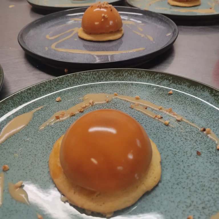 Assiette entremet caramel avec glaçage brillant réalisé en formation pâtisserie. Dessert sphérique en caramel sur un biscuit, décoré de sauce.