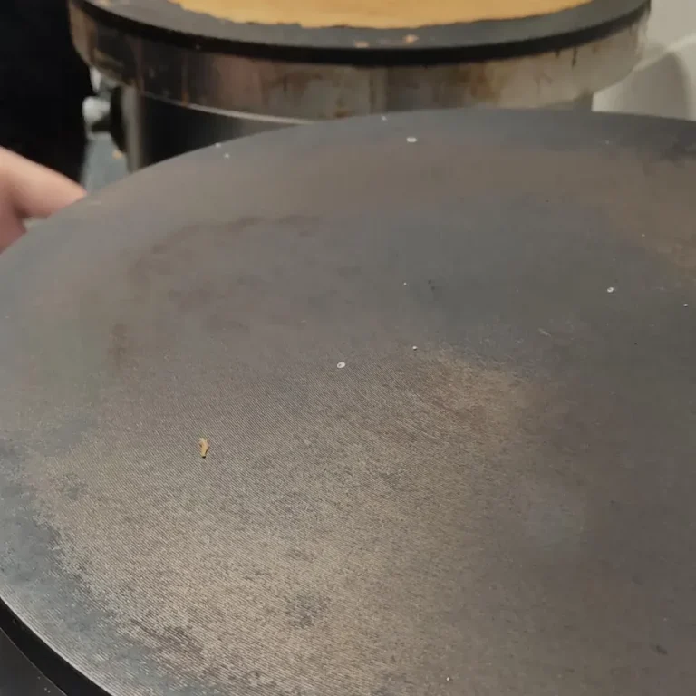 Techniques du crêpier Une crêpe dorée cuite sur une crêpière, avec des mains en arrière-plan.