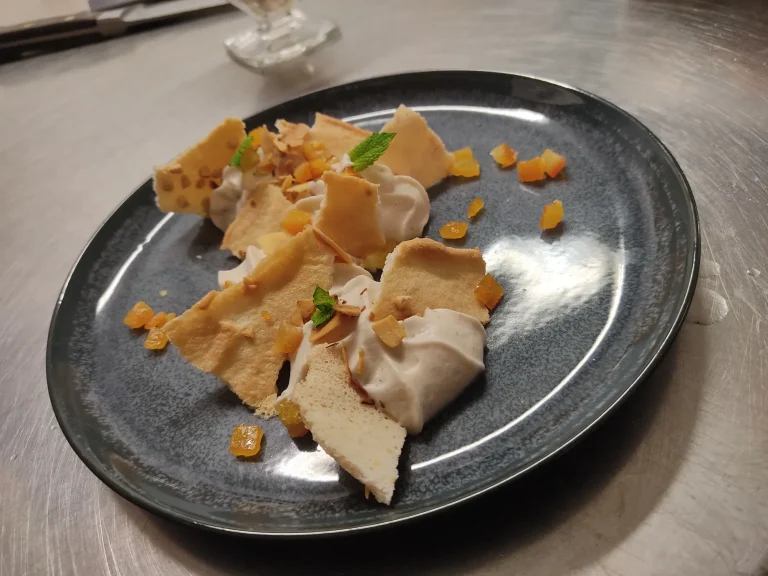 Mousse et tuiles meringuées Dessert élégant avec des morceaux de meringue et de la crème sur une assiette noire.