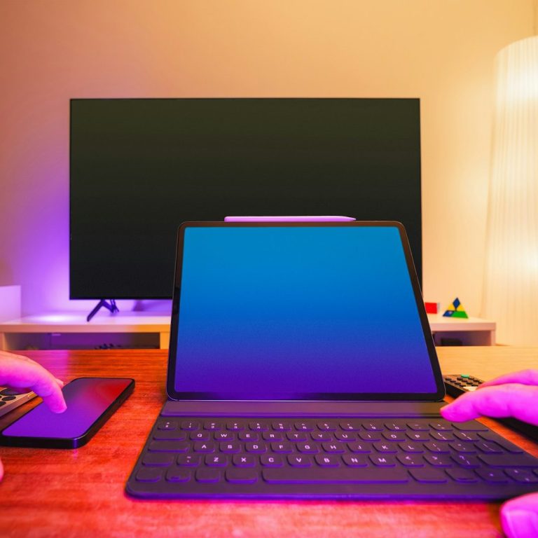 Trois écrans de différentes taille Bureau avec un ordinateur portable, un téléphone et un téléviseur en arrière-plan éclairé.